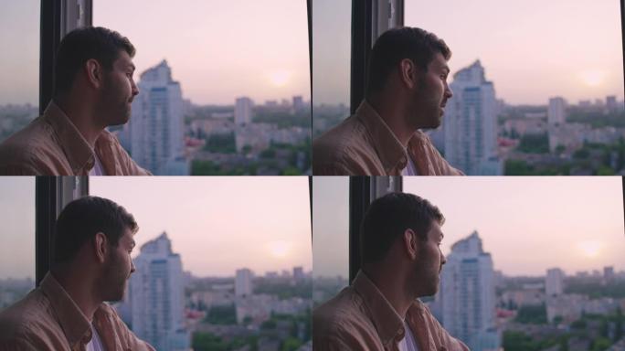 悲伤的中年男子站在窗户旁看着城市景观，对问题感到不安