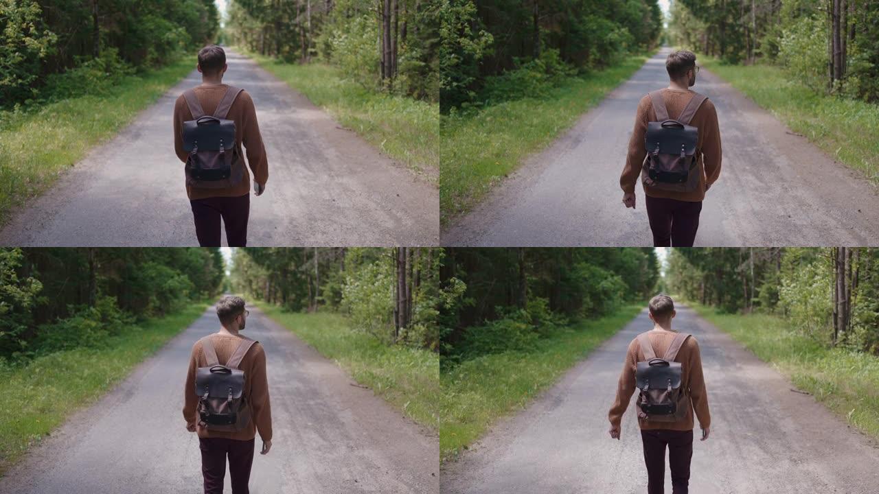 一个背着背包的游客正沿着森林地区的道路行走，环顾四周。后视图