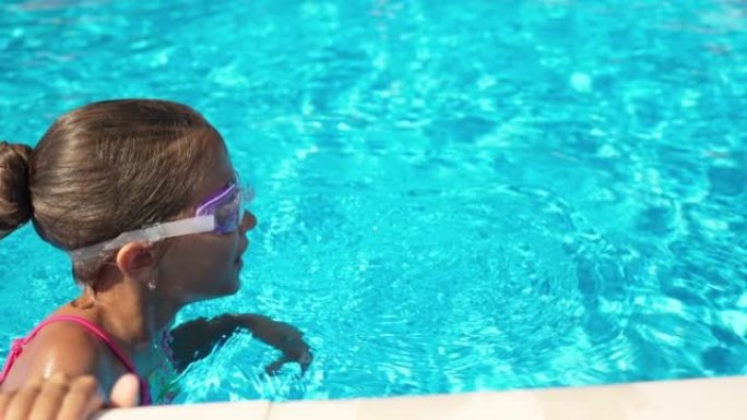夏天，一个穿着紫色眼镜的粉红色泳衣的女孩漂浮在蓝色水的游泳池上