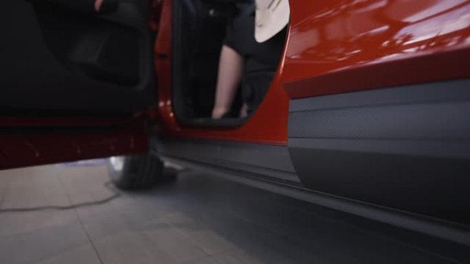 一个陌生的女人坐在驾驶座上，用慢动作关上红色车门。自信优雅的女性买家在经销商选购新车。购买和消费观念