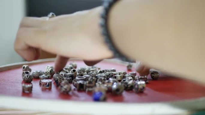 一个戴着戒指和手链的女人，在一家珠宝店挑选银饰，倒出一堆链接，组装成一个银饰链。特写镜头