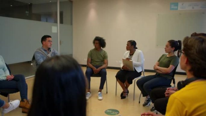 一群不同的学生坐在一个圆形与黑人女性顾问咨询会议