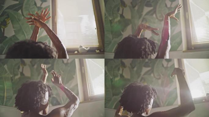 美丽的非洲民族妇女在现代浴室放松。享受透过窗户的阳光。举起湿手