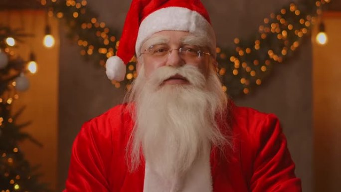 头像看着相机快乐的老大胡子圣诞老人穿着服装，挥舞着视频变焦，录制视频圣诞快乐的问候，面对相机视图。