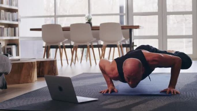 运动员在家庭锻炼期间做俯卧撑运动。使用笔记本电脑