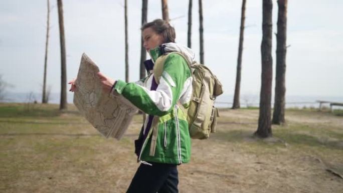 带纸质地图的侧视图女人在荒野中慢动作行走。高加索女性游客探索户外自然，背包漫步。旅行和旅行概念。