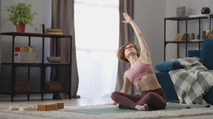 成年运动型女性周末在家锻炼，坐在房间的地板上练习瑜伽