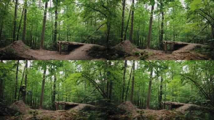 Camera zoom back是一个专业的山地自行车骑行者在绿色森林中高速跳过障碍物和蹦床的电影镜
