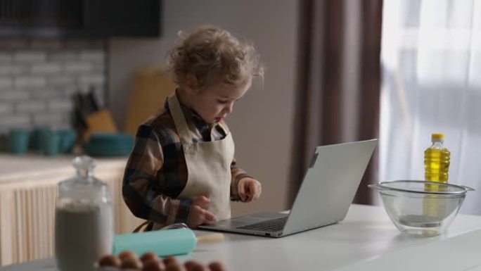小男孩正在学习烹饪，在笔记本电脑上观看儿童教程，独自在家庭厨房玩耍，中等肖像
