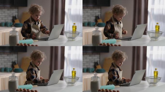 小男孩正在学习烹饪，在笔记本电脑上观看儿童教程，独自在家庭厨房玩耍，中等肖像
