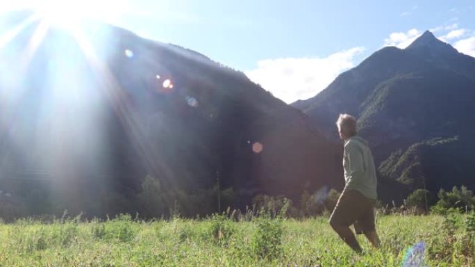 男人在日出时越过绿色草地，遥远的山脉