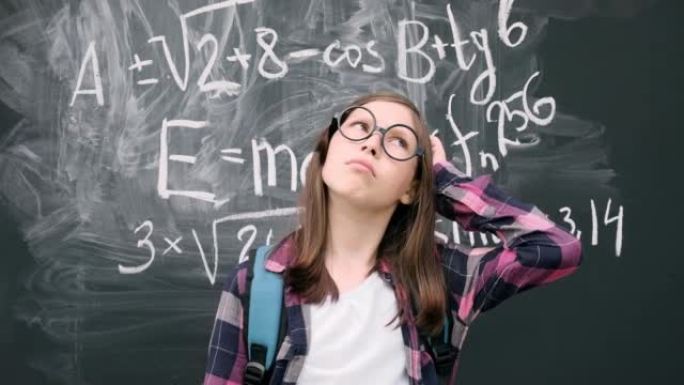 戴着眼镜和蓝色背包的少女女学生站在黑板背景上思考。然后她用手指指着，因为找到了答案。头脑风暴和明亮的