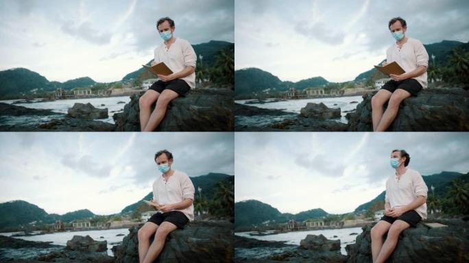 一名戴着面具的男子坐在海洋附近的岩石上写书的特写镜头