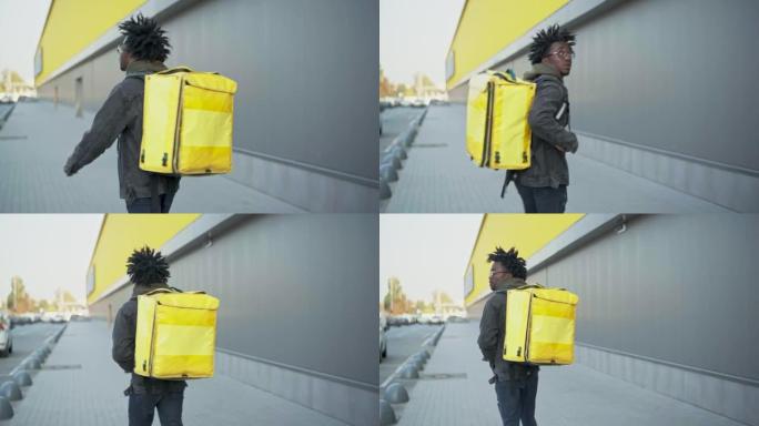 年轻的非洲裔美国快递员带着黄色保温袋在户外四处张望。在送货服务学习后工作的男生。自信和生活方式。
