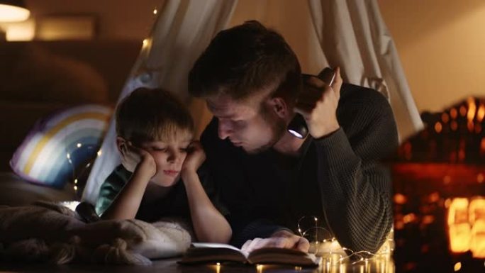 小儿子和爸爸在房间的帐篷里，晚上用手电筒看书，父亲和孩子