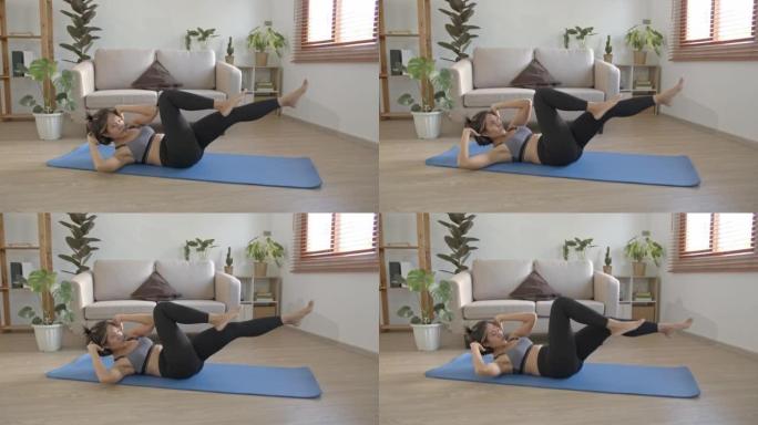 亚洲年轻女子躺在地板垫上，做仰卧起坐的自行车紧缩运动，以改善腹肌并在家中减少脂肪。
