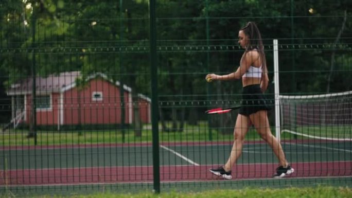 马尾辫性感的运动型女士独自在网球场上训练，用球拍走路和击球