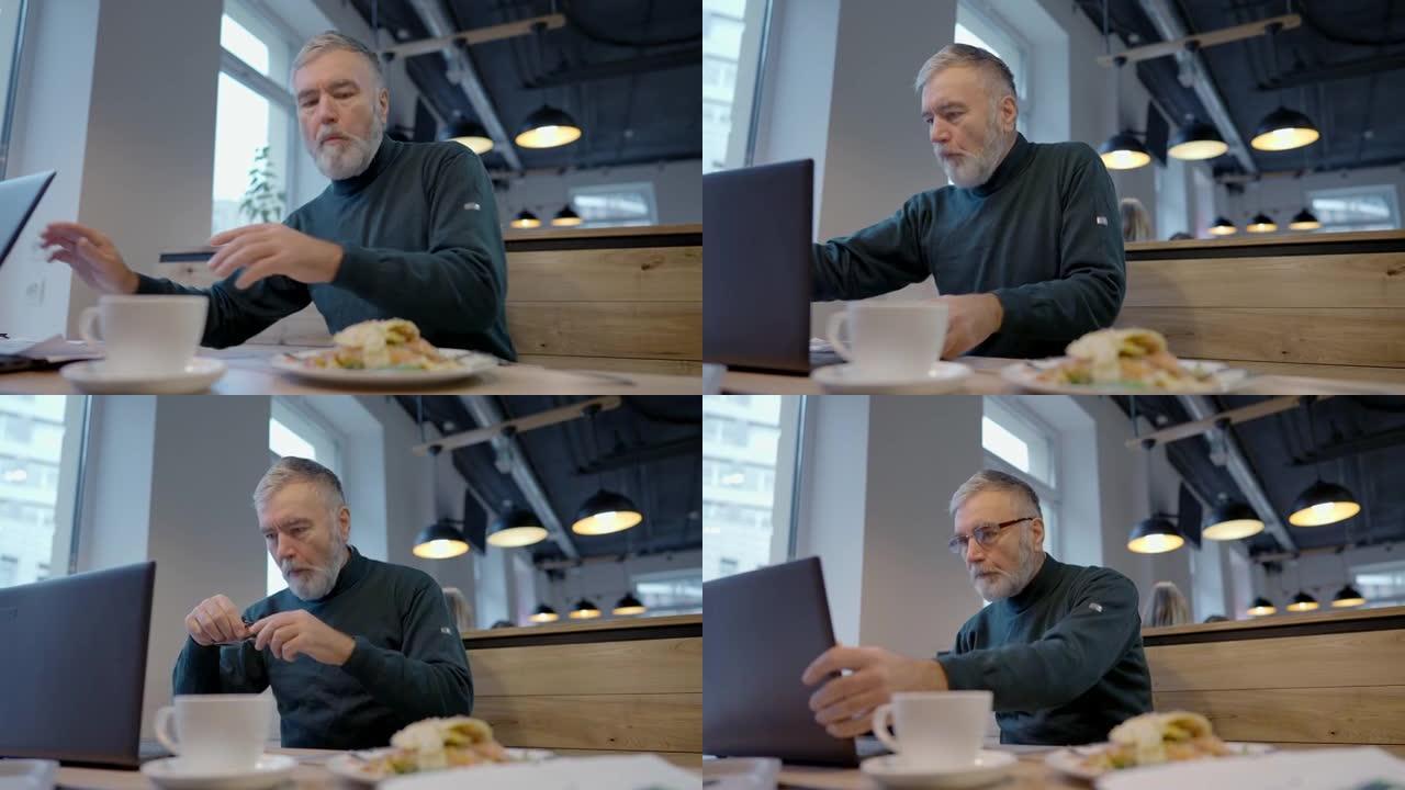 忙碌的高加索高级商人在餐厅用餐，戴眼镜并在笔记本电脑上接听视频电话的肖像。自信成功的人在午休时过度劳