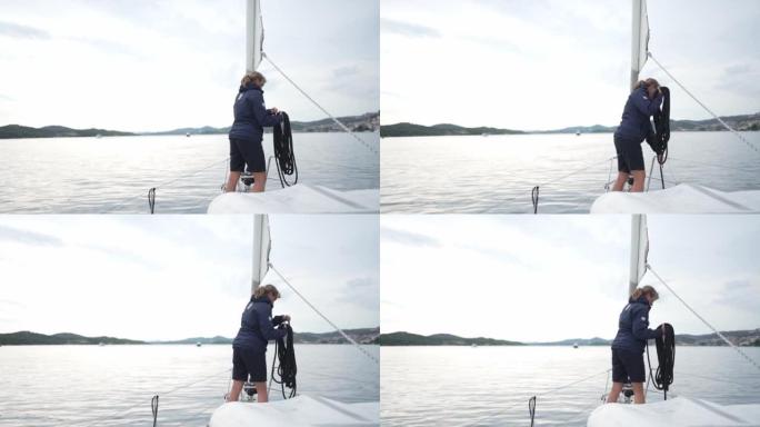 一个女人倾向于在平静的海湾上的帆船上系绳