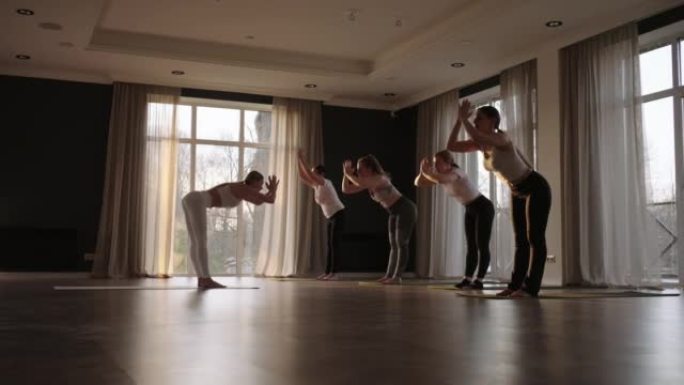 在慢动作中，一群女性一起做不同年龄和体重类别的瑜伽，瘦胖的女性在早晨的健身房里晒太阳。太阳在地板上的