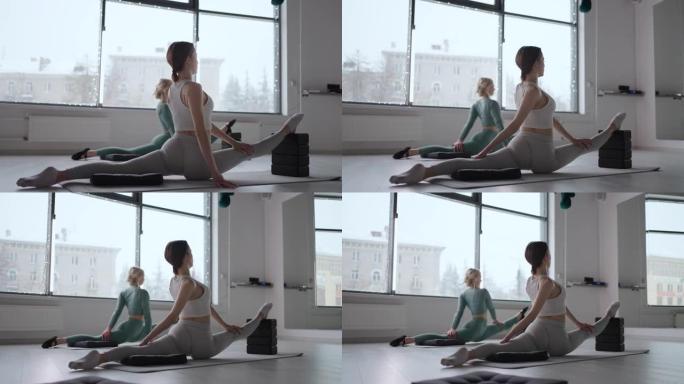 窗户背景下的两个女人在体育工作室里做伸展运动。伸展运动。妇女从普拉提 (Pilates) 进行健康锻