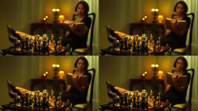 特写棋盘，背景模糊的女玩家看书，脚坐在桌子上。红发高加索苗条体贴的女人在家室内计划游戏策略。