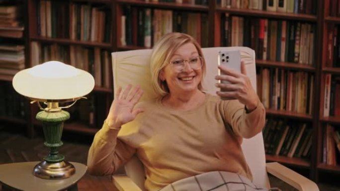 快乐的高级女人在智能手机相机上挥舞着手，在网上与朋友交谈