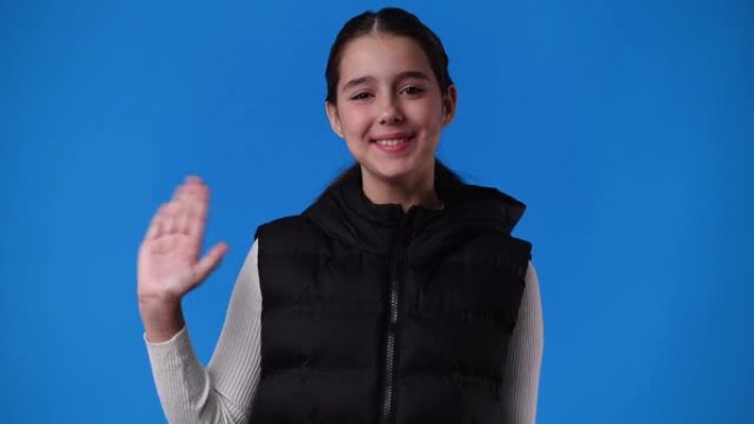一个女孩在蓝色背景上挥手打招呼的4k视频。