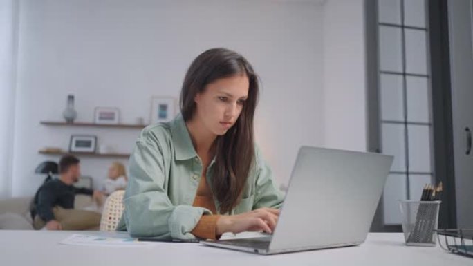 一名女商人在家里用笔记本电脑远程工作，在家人唱歌的背景下通过网络摄像头展示图表。忙碌的女商人。家庭办