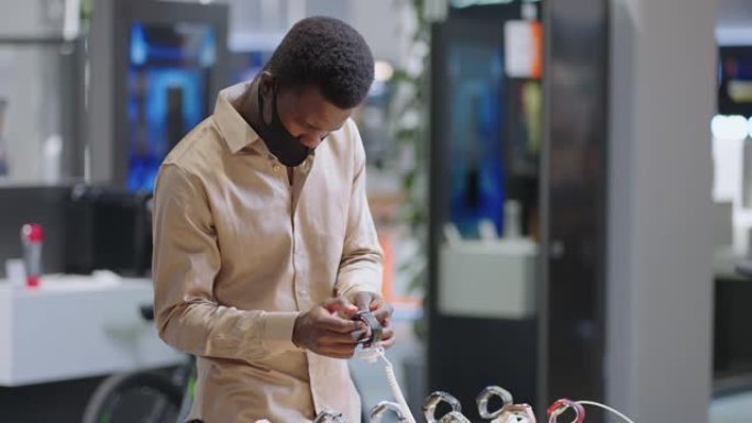 戴着口罩的非洲裔美国人正在电子商店测试智能手表，在大型商店购买现代设备