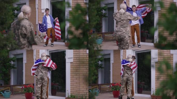 广角镜头，快乐的少年与美国国旗跳舞的慢镜头站在门廊，快乐的女兵身穿迷彩服，拥抱少年跑向儿子。激动的户