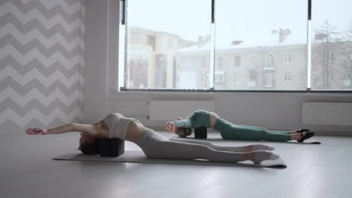 两名苗条的年轻妇女躺在立方平台上进行背部锻炼。背部肌肉的伸展和张力。姿势的改善