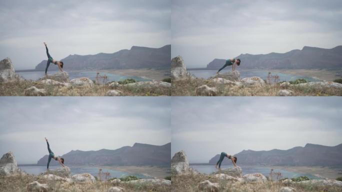 年轻女子在海滩附近的悬崖上的岩石上做瑜伽