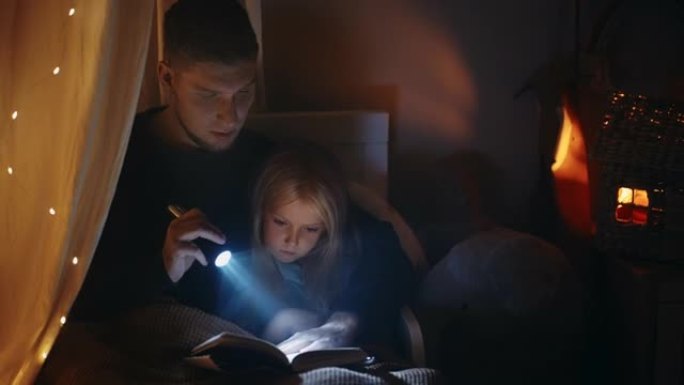 小女孩和她的父亲在黑暗中读书，在页面上闪耀手电筒，听童话