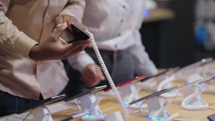 美国黑人男女正在数字设备商店购物，从演示展示柜中提取智能手机的展览样本，双手特写