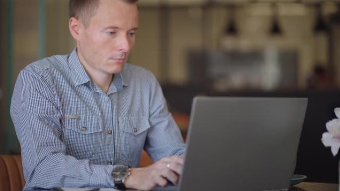 一个穿着衬衫的年轻人坐在笔记本电脑的桌子旁，在键盘上打字。学生可以远程学习。一个商人远程做生意