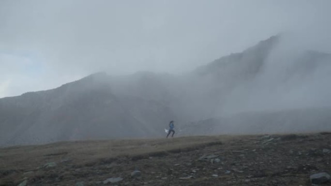 女越野跑运动员在草地上的雾气中奔跑，后面是白雪皑皑的山峰