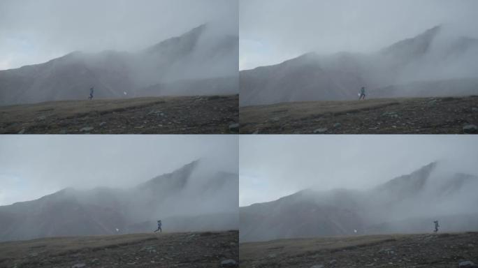 女越野跑运动员在草地上的雾气中奔跑，后面是白雪皑皑的山峰