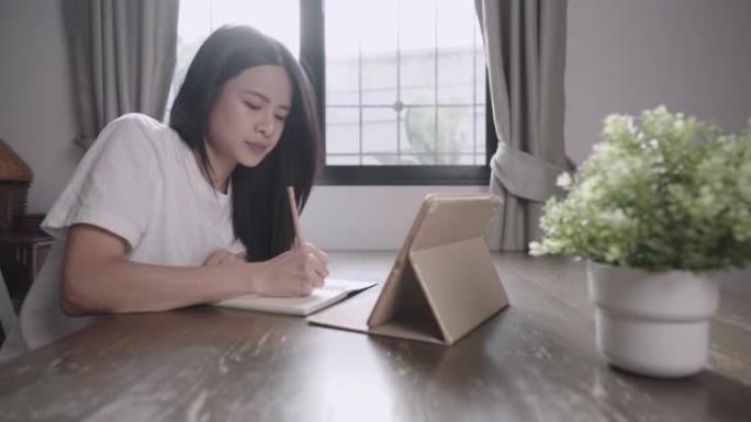 年轻的亚洲女孩正在做期末考试复习，在网上上课，在家上学，用铅笔在小笔记本上写下，找工作的机会，独自坐