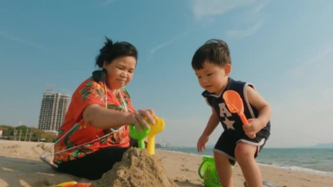 亚洲蹒跚学步的男孩正在海滩上建造沙堡