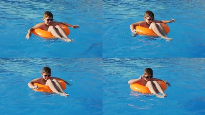 游泳池里一个开朗可爱的男孩戴着墨镜坐在一个游泳的橙色圆圈里游泳，把头移到音乐的节奏上，在日落时拍手在
