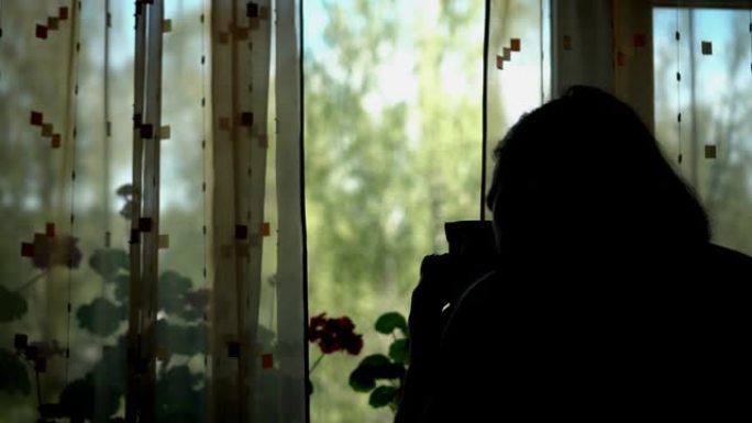 一个男人站在窗前，拿着一台旧电影摄影机的剪影。他的身影在光窗的背景下可见