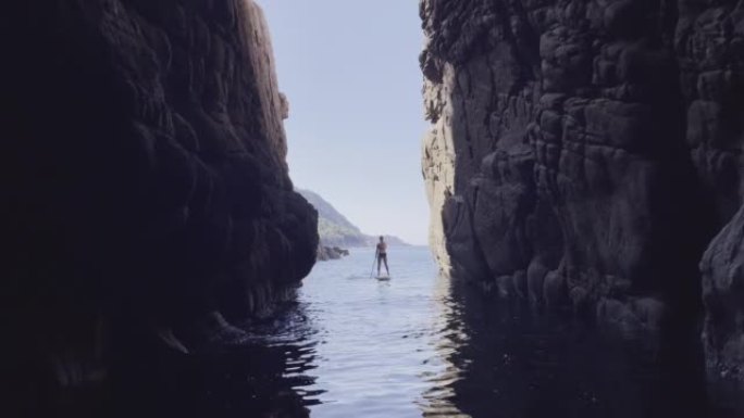 一名妇女在大岩壁附近的水上桨板上划桨的广阔视野