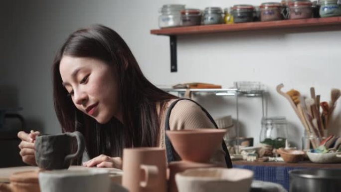 年轻女子在陶器工作室用粘土覆盖和装饰陶瓷。波特女孩在烤粘土上画颜色。教育、商业、艺术天赋和创意手工制