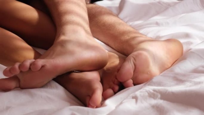在床上休息的男人和女人的腿的特写。早上在温暖的毯子下恋爱的情侣