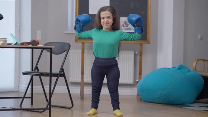 微笑的高加索女性小人物撞拳击手套打手势力量看着站在室内的相机。带有基因突变姿势的自信女人的肖像。武术