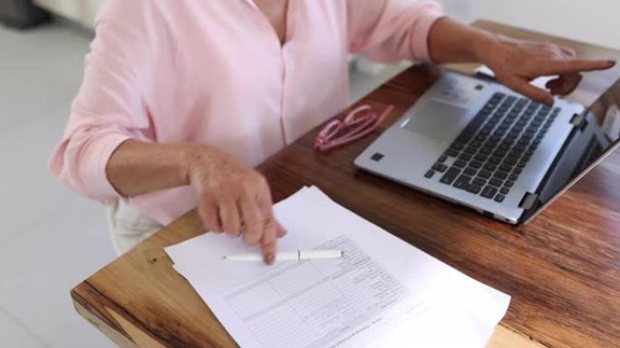 企业家高级妇女用笔记本电脑列出客户名单，在家工作时在纸上写字