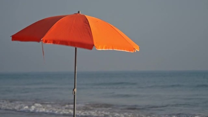 一把橙色的沙滩伞对着海浪，以慢动作射击。
