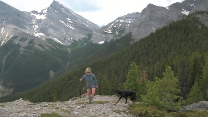 女徒步旅行者带着狗到达山脊，远处的山脉