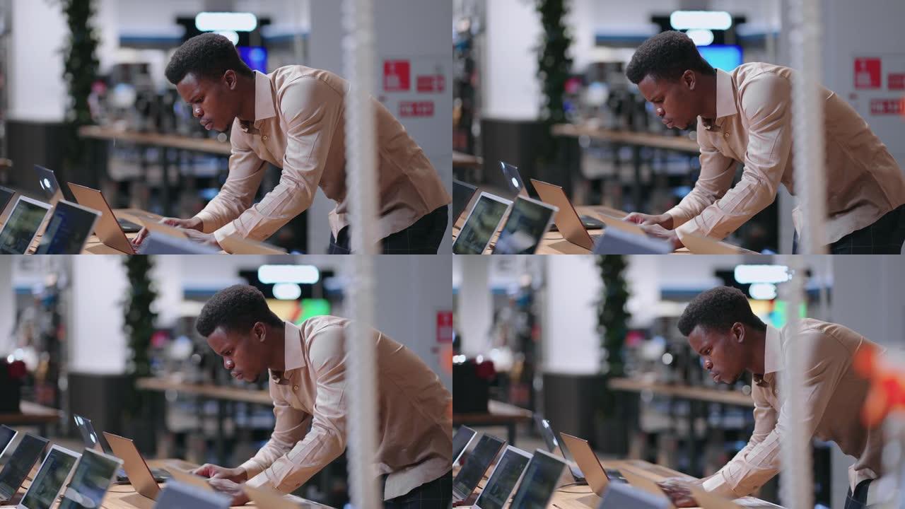 年轻的黑人程序员正在选择新的笔记本电脑在电子商店工作，测试展览样本